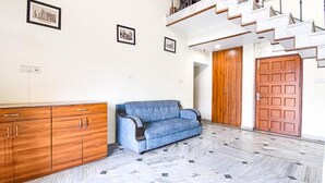 A living room with a blue sofa, wooden cabinets, a staircase, and a wooden door. - Fabexpress Duplex Villa (Barasat)