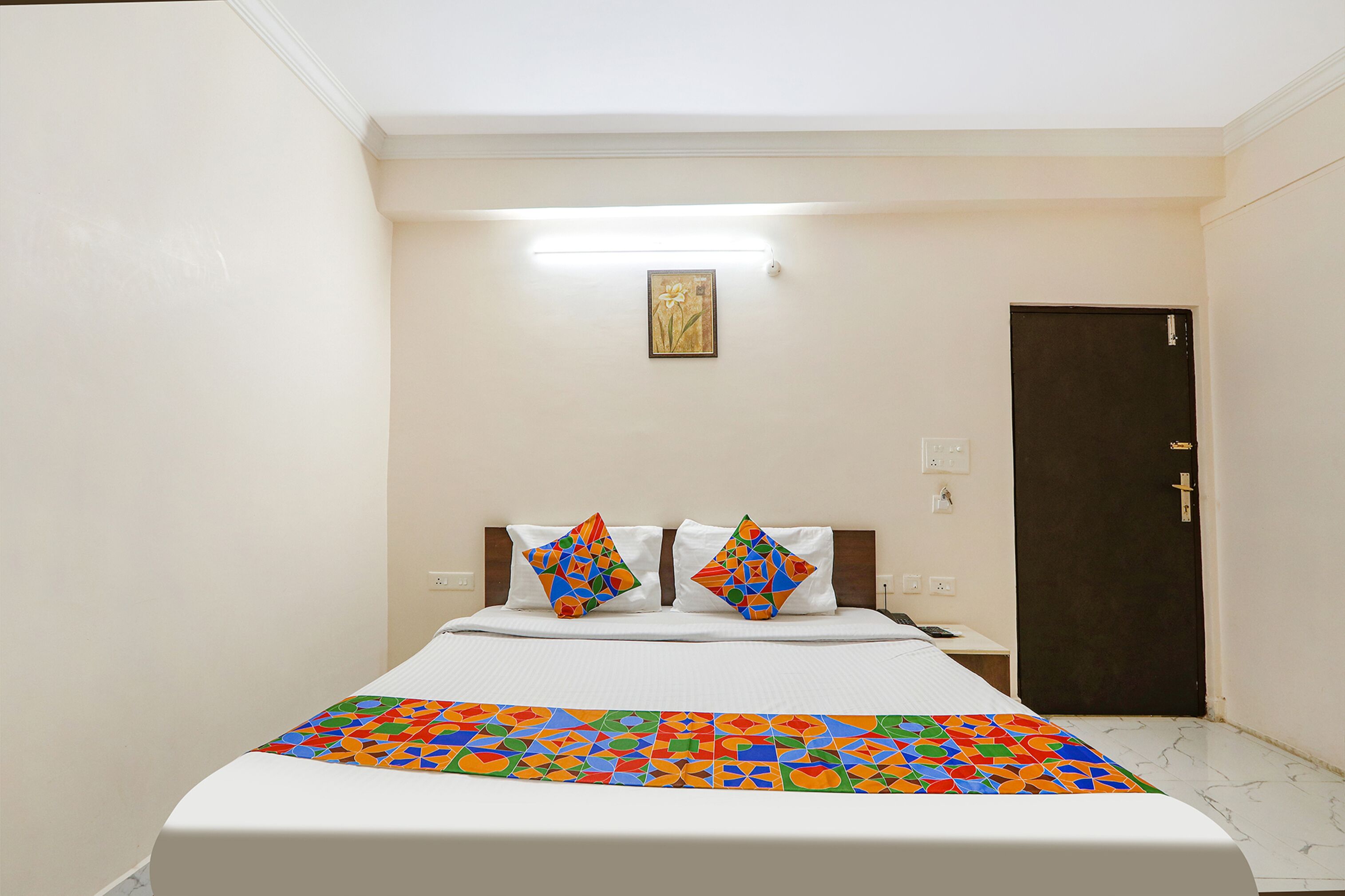 A hotel room with a bed, a nightstand, a door, and a wall-mounted light fixture.