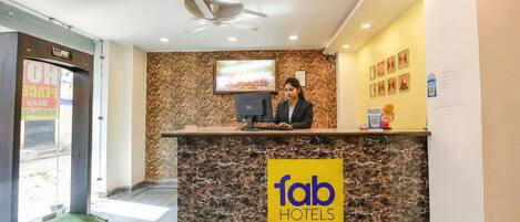 A hotel reception desk with a marble counter, a ceiling fan, and a TV screen.
