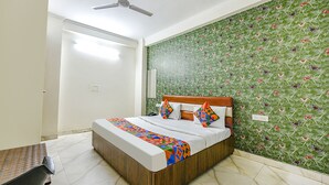 A bedroom with a bed, a wooden headboard, a patterned wall, and a ceiling fan. - Via Peaceful Stay Palam (New Delhi)