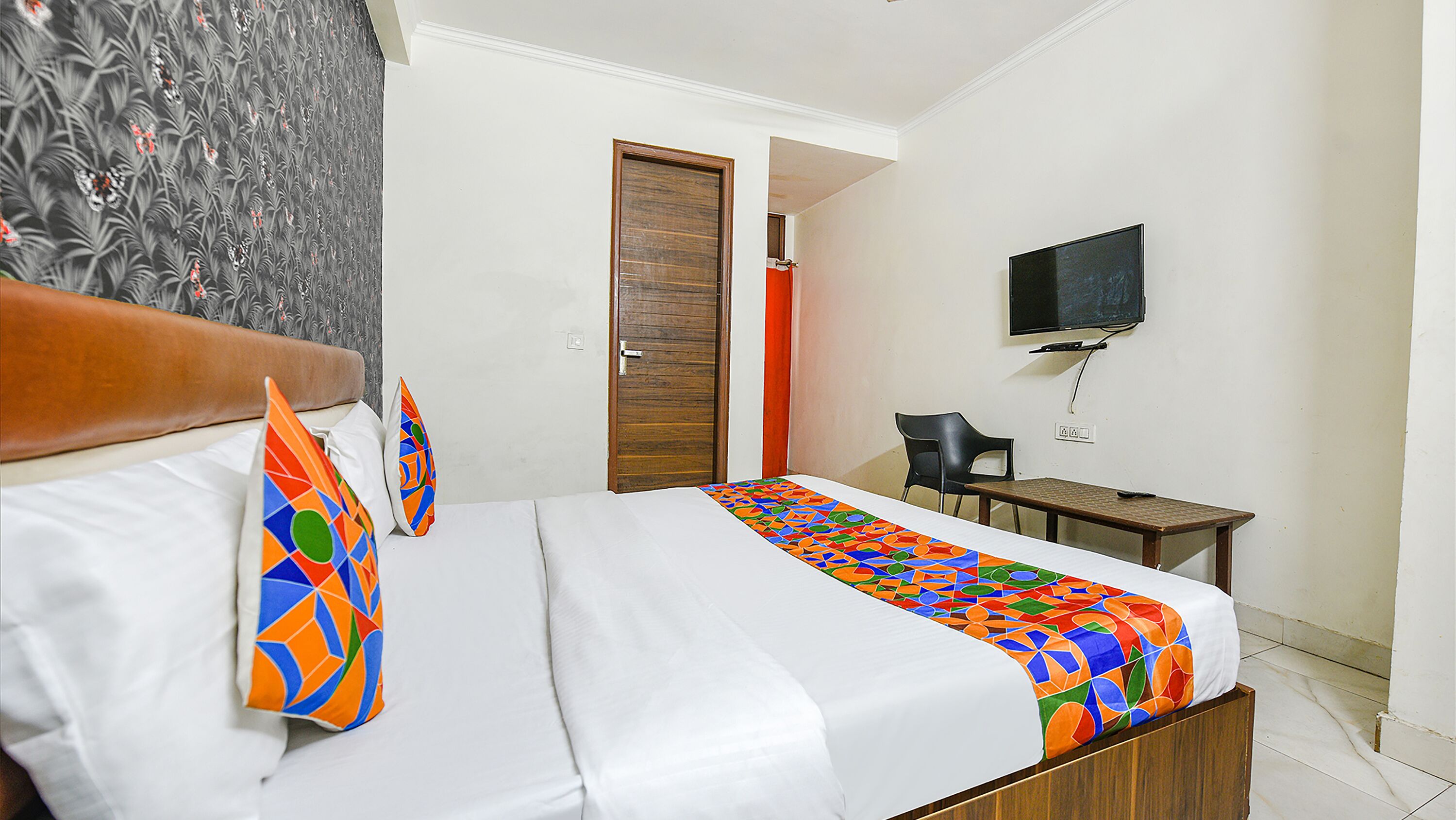 Une chambre d’hôtel avec un lit, un bureau, une chaise, une télévision et une porte.