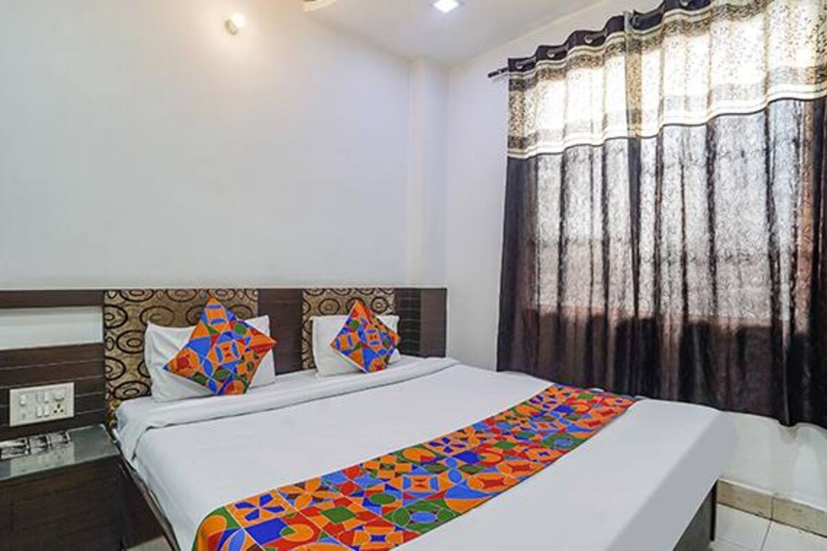 Una habitación de hotel con una cama bien hecha, una mesita de noche y una ventana con cortinas.