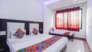 A hotel room with two beds, a large window with red curtains, and a colorful quilt on the beds. - Fabexpress Taj Prince (Agra)
