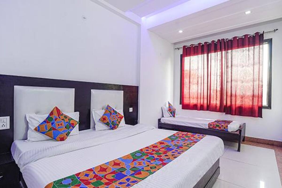 Una habitación de hotel con dos camas, un ventanal con cortinas rojas y un colcha colorida sobre las camas.
