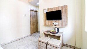 Una habitación pequeña y limpia, con un mueble bajo de madera para el televisor, un televisor de pantalla plana, una mesita con un hervidor y dos taburetes acolchados.