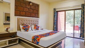A hotel room with a large bed, a brick accent wall, a sliding glass door to the balcony, and a small bedside table. - FabHotel The Royal Heritage (Mahabaleshwar)