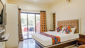 A hotel room with a large bed, a television, a desk, and a view of the outdoors. - FabHotel The Royal Heritage (Mahabaleshwar)
