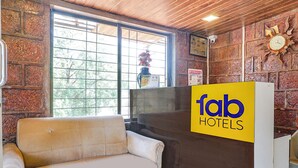 A reception area with a sofa, a clock, and a window with a view of trees. - FabHotel The Royal Heritage (Mahabaleshwar)