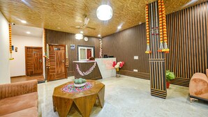 A reception area with a wooden reception desk, a round wooden table with a floral centerpiece, and a sofa. - Fabhotel Lake View Ii (Dehradun)