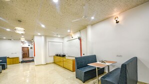 A spacious room with a high ceiling, a blue sofa, a small table, and a wooden cabinet. - Fabhotel Lake View Ii (Dehradun)