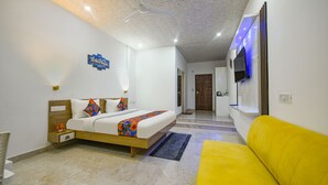A bedroom with a bed, a yellow sofa, a ceiling fan, and a TV mounted on the wall. - Fabhotel Lake View Ii (Dehradun)