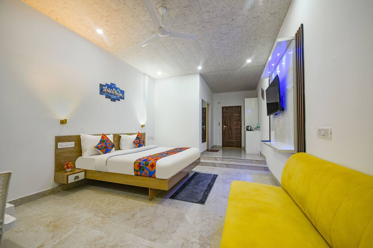 A bedroom with a bed, a yellow sofa, a ceiling fan, and a TV mounted on the wall.