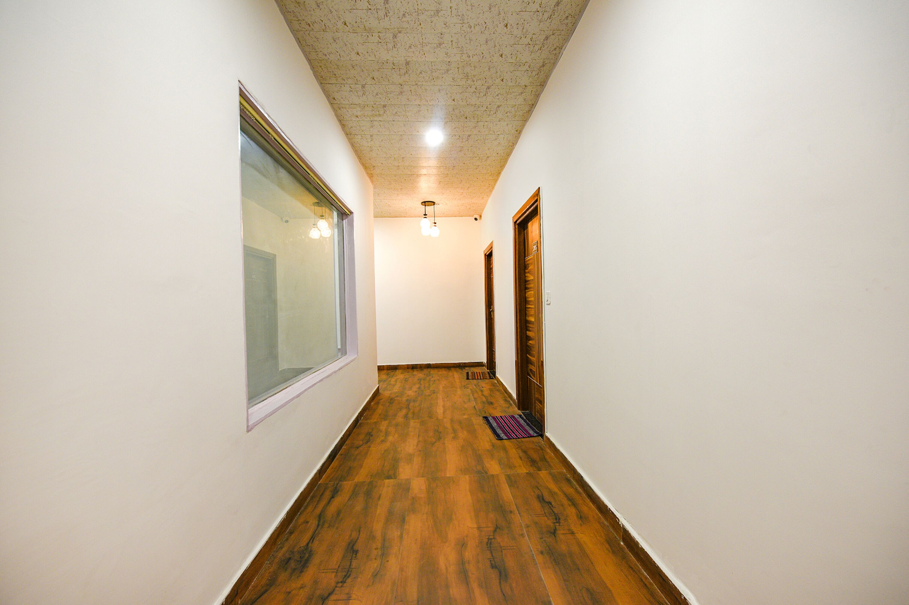 A narrow hallway with wooden flooring, white walls, and a ceiling with recessed lighting.