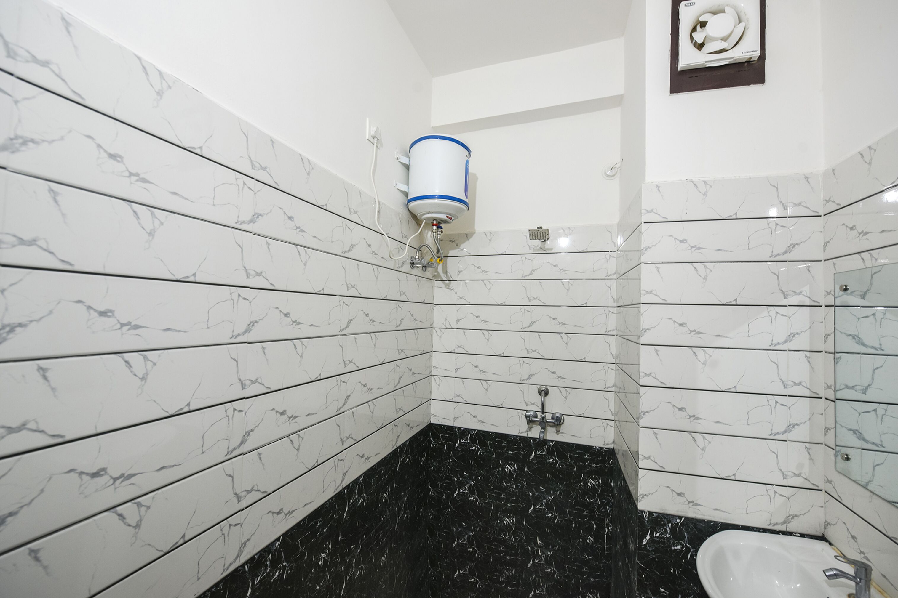 A bathroom with white marble tiles, a black marble floor, a toilet, and a hand dryer mounted on the wall.