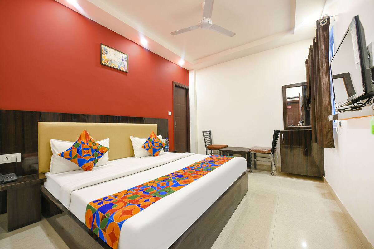 Quarto de hotel com cama, escrivaninha, cadeira, televisão e ventoinha no teto.