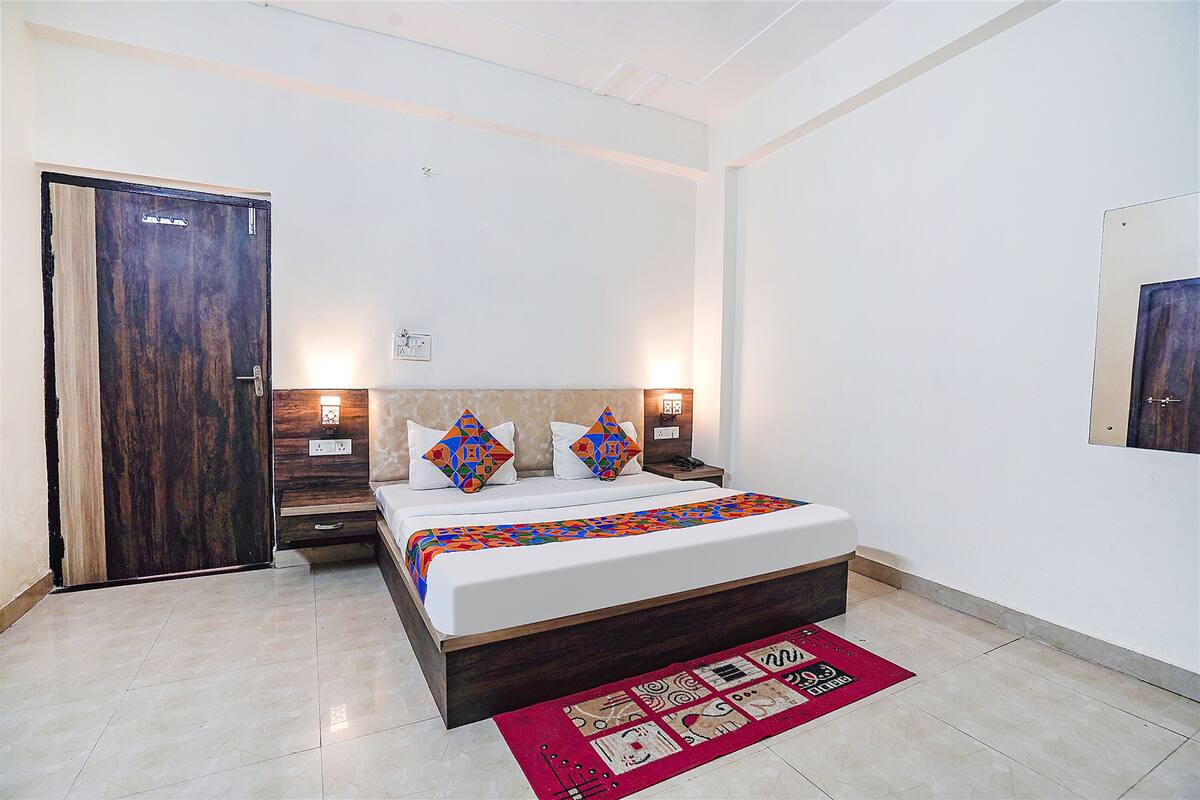 A bedroom with a bed, nightstands, a wooden door, and a red patterned rug.