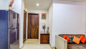 A living room with a sofa, a wooden door, a small table with a vase, and a refrigerator. - Fabexpress Spandan Inn (Barasat)