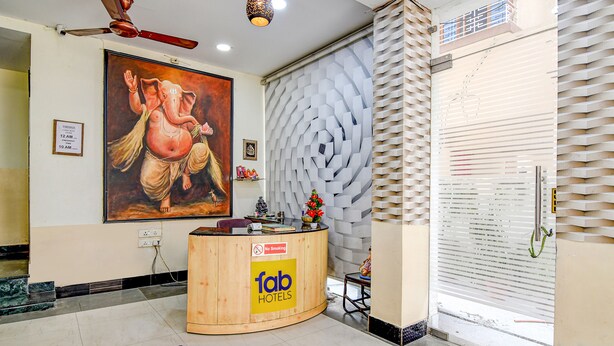 A hotel reception area with a wooden desk, a large painting of an elephant, and a modern wall design. - Fabexpress Spandan Inn (Barasat)