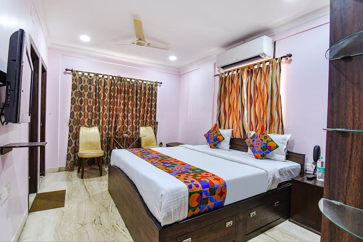 A hotel room with a bed, a chair, a desk, an air conditioner, and a ceiling fan.
