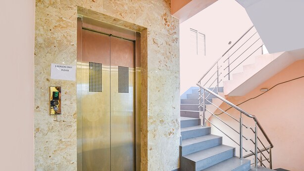 Ein Aufzug mit einem Schild, das die Nutzung nur für 3 Personen erlaubt, neben einer Treppe mit Metallgeländer.