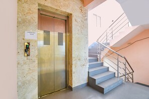 An elevator with a sign indicating it is for 3-person use only, next to a staircase with a metal railing.