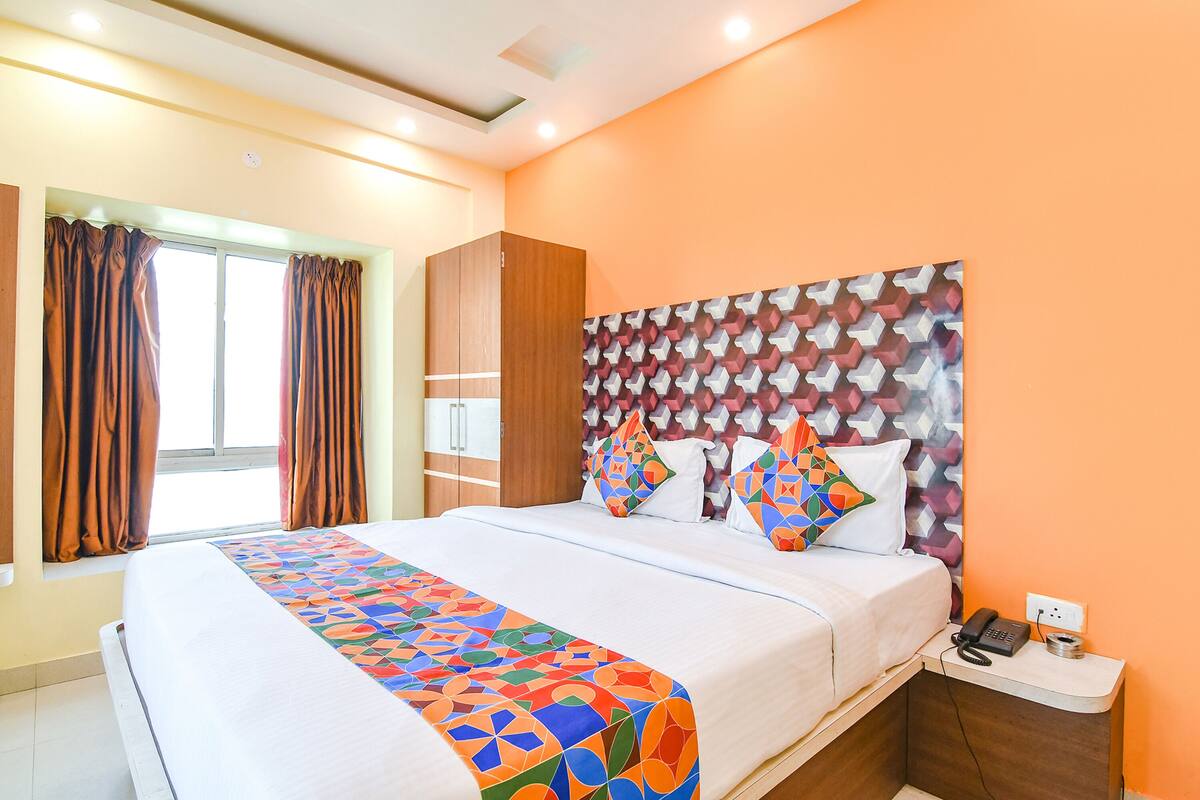 A hotel room with a large bed, a nightstand with a phone, and a window with curtains.