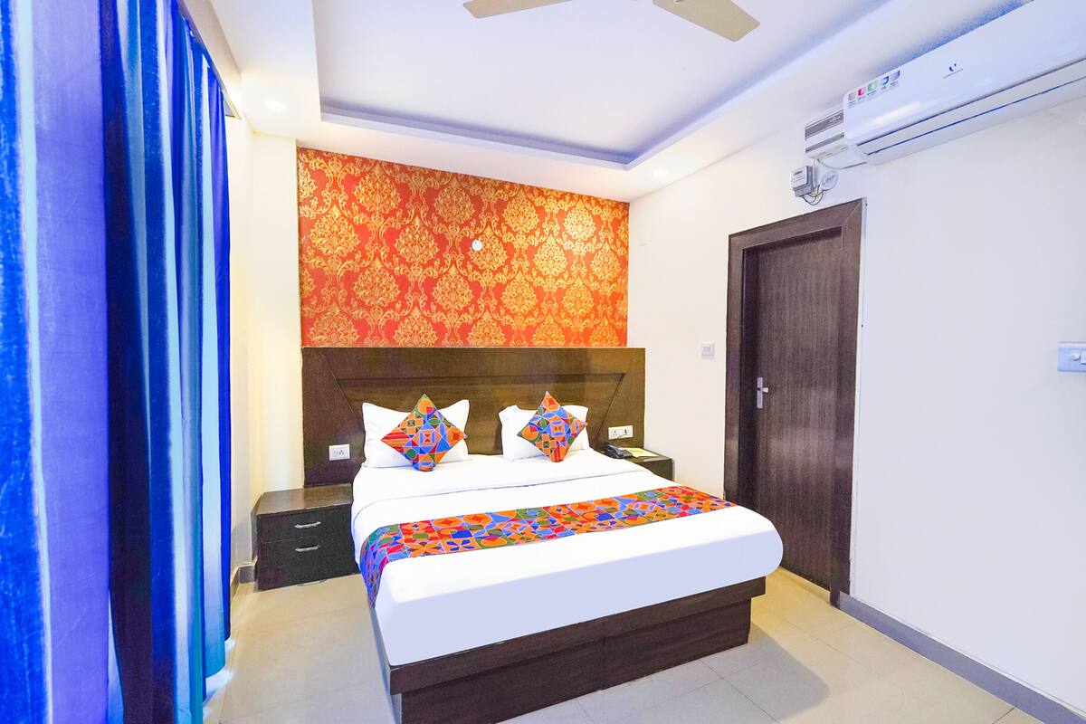 A hotel room with a large bed, a wooden headboard, a nightstand, a bedside table, a wardrobe, and a ceiling fan.