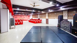 Um salão amplo com palco, fileiras de cadeiras vermelhas e um ventilador de teto.