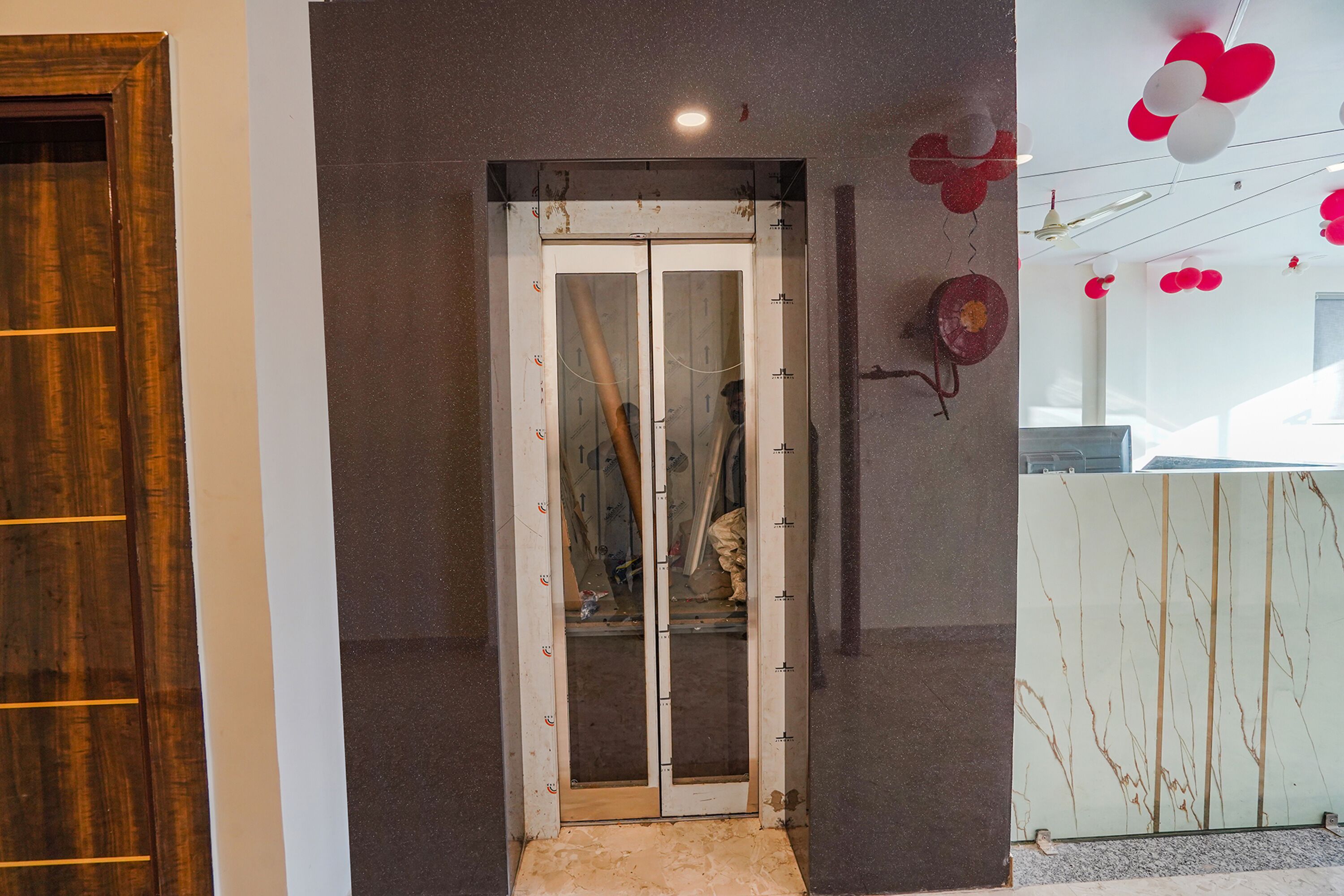 A room with a wooden door, a glass elevator, and a decorative wall with red and white balloons.