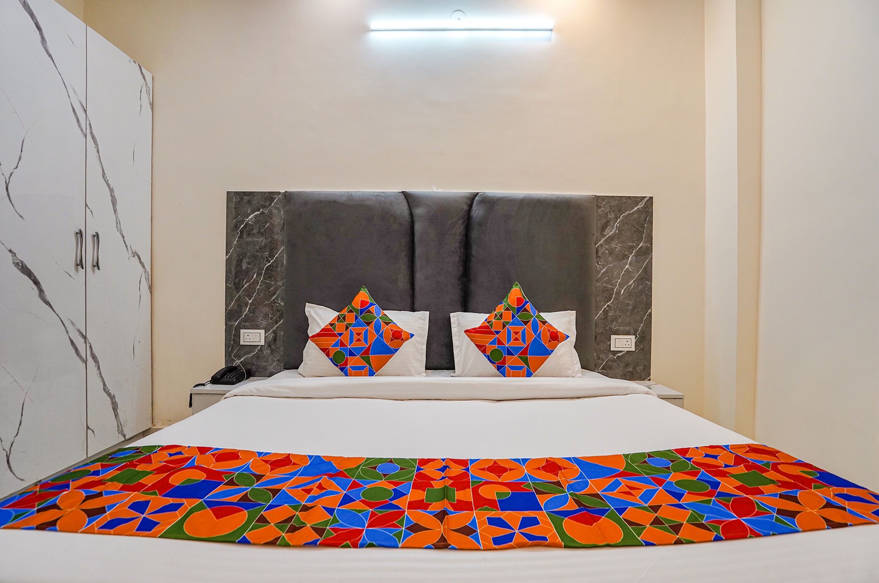 A hotel room with a bed, a nightstand, a telephone, a marble wardrobe, and a patterned bedspread.