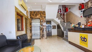 A hotel lobby with a reception desk, a staircase, a sofa, and a glass coffee table. - Fabhotel Spb 87 (New Delhi)