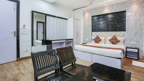 A modern hotel room with a bed, a desk, a chair, a small table, a mirror, and a ceiling fan. - Fabhotel Spb 87 (New Delhi)
