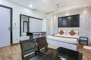 A modern hotel room with a bed, a desk, a chair, a small table, a mirror, and a ceiling fan. - Fabhotel Spb 87 (New Delhi)