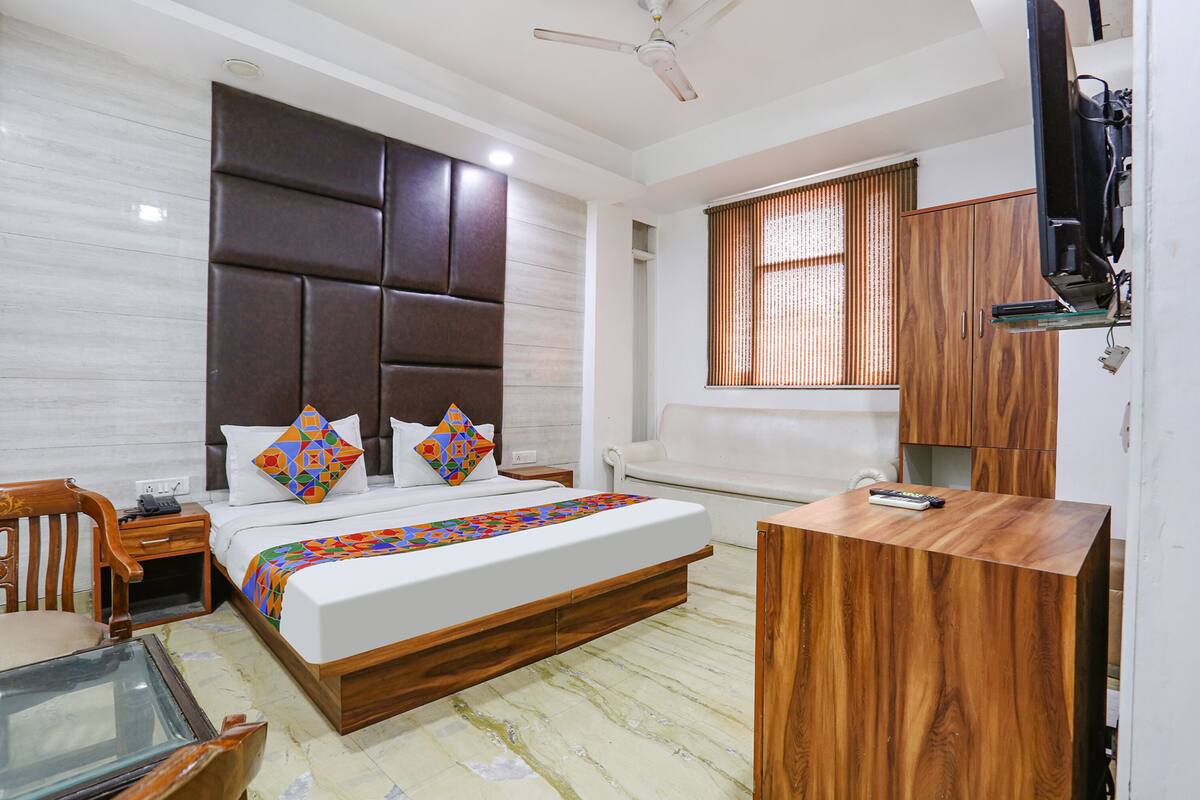 A bedroom with a bed, wooden headboard, bedside table, and a TV mounted on the wall.