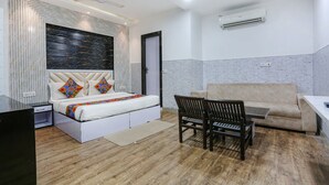A modern hotel room with a bed, a sofa, a dining table, and a chair. - Fabhotel Spb 87 (New Delhi)