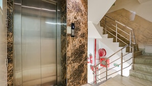 An elevator, a marble wall, and a staircase with metal railings and a fire extinguisher. - Fabhotel Spb 87 (New Delhi)