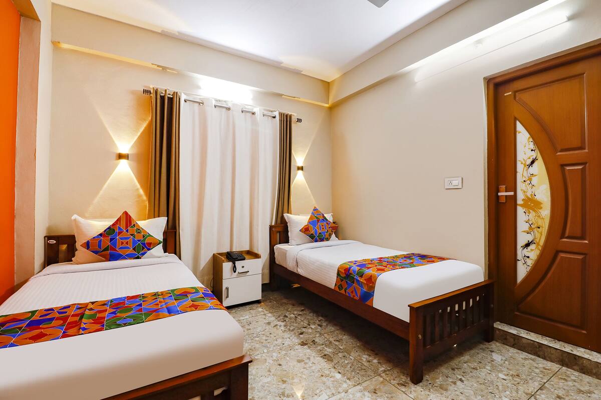 A hotel room with two beds, a nightstand, a wooden door, and a bathroom with a shower curtain.