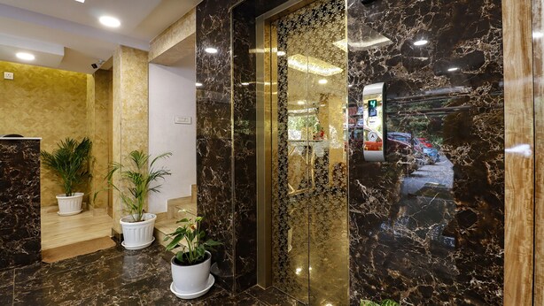 Un vestíbulo con suelo de mármol, plantas en macetas y un ascensor de vidrio.