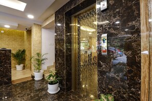 A lobby with marble flooring, potted plants, and a glass elevator. - Fabhotel Dreams Paradise Airport Residency (Aluva)
