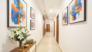 A hallway with framed abstract paintings on the walls, a wooden console table with a vase of flowers, and a door at the end. - FabHotel Hari Kunj 900 m from Kashi Vishwanath Temple (Varanasi)