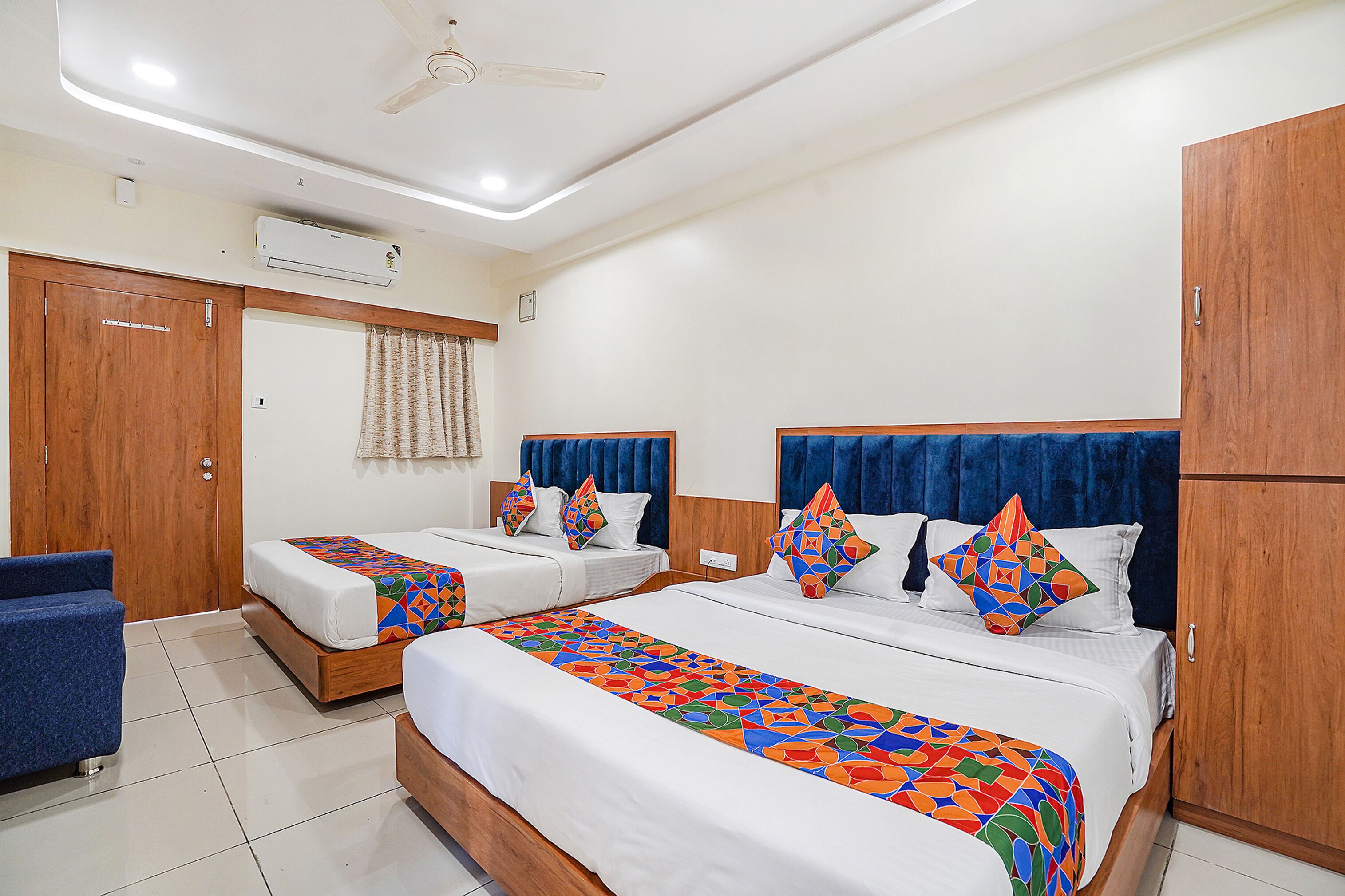 A hotel room with two beds, a wardrobe, an air conditioning unit, and a ceiling fan.