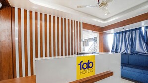 A reception desk with a 'fab hotels' sign, wooden slats, a blue sofa, and a ceiling fan. - Fabhotel Hk Villa (Vadodara)