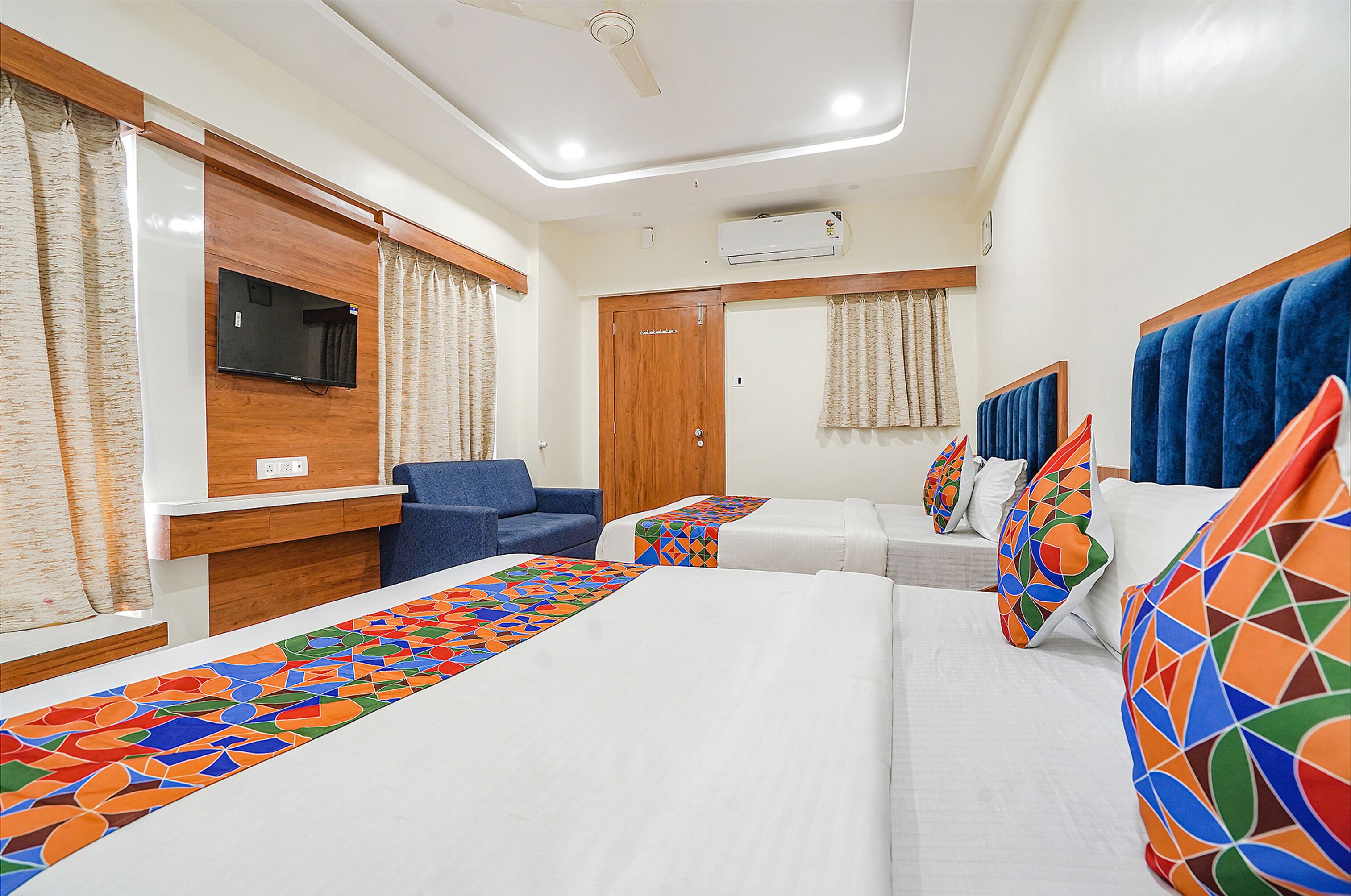 Habitación de hotel con cama, sofá, televisión y ventana con cortinas.