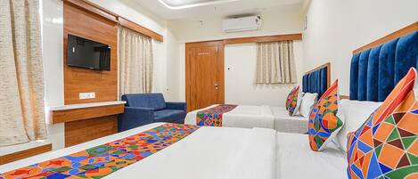 Habitación de hotel con cama, sofá, televisión y ventana con cortinas.