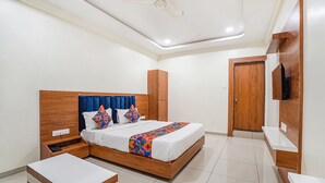 A bedroom with a wooden bed, a bedside table, a nightstand, a TV, and a wardrobe. - Fabhotel Hk Villa (Vadodara)