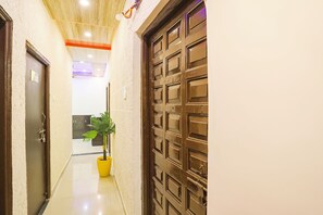 A hallway with a wooden door, a potted plant, and a tiled floor. - Fabhotel Universal Stay Inn (Nagpur)