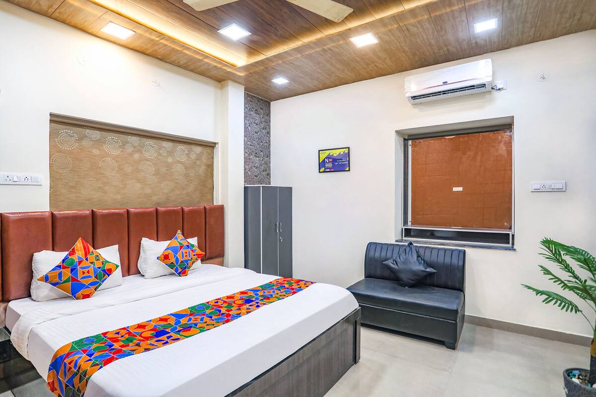 A hotel room with a bed, a sofa, a wardrobe, an air conditioner, and a window.
