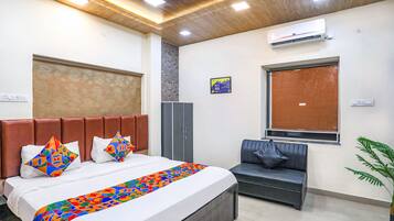 A hotel room with a bed, a sofa, a wardrobe, an air conditioner, and a window.