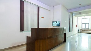 Un área de recepción con un mostrador de madera, un televisor montado en la pared y un ventanal con persianas.