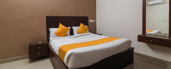 A neatly made bed with a white and orange bedspread, two matching pillows, a wooden headboard, a nightstand with a drawer, and a mirror above the bed. - Fabexpress R Inn (Hyderabad)